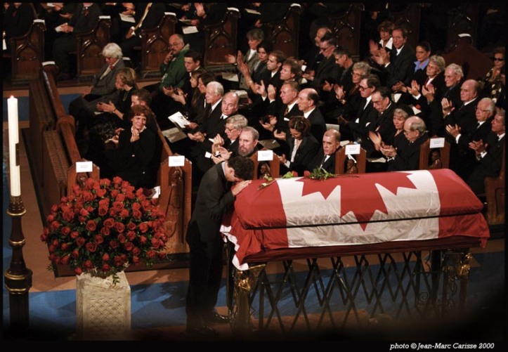 The photograph shows former Prime Minister Pierre Elliott Trudeau’s family, friends, colleagues, and official guests in attendance to observe his passing. His son, Justin, now the Prime Minister of Canada, rests his head on the casket of his father. Margaret Trudeau, in the front pew with son, Alexandre, is flanked by the beloved prime minister’s later life partner, Deborah Coyne, and their daughter, Sarah. The former prime minister’s sister, Suzette Rouleau, is on the far side of the same first row. Leonard Cohen on the right. In attendance next to Cuban President Fidel Castro are former Governor-General Romeo Leblanc, His Highness Prince Karim Aga Khan and former U.S. President Jimmy Carter. Other notables present at the ceremony not shown in this photograph include past Canadian Prime Ministers John Turner, Joseph Clark, Brian Mulroney, and Jean Chrétien. Photo: Copyright Jean-Marc Carisse.